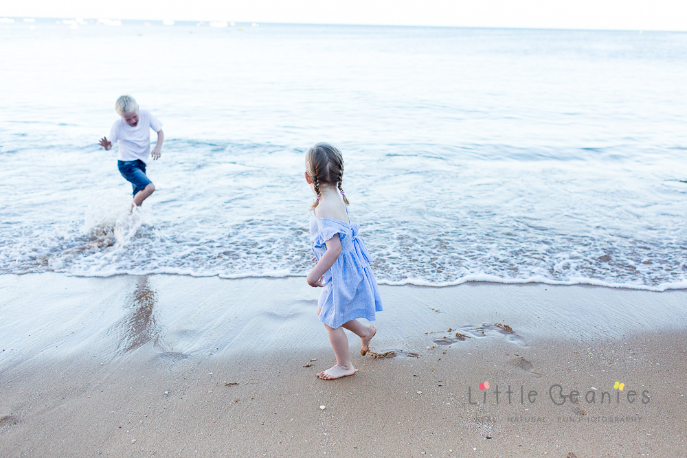 brother and sister playing on the beach and splashing in the waves whilst having their professional family photo taken