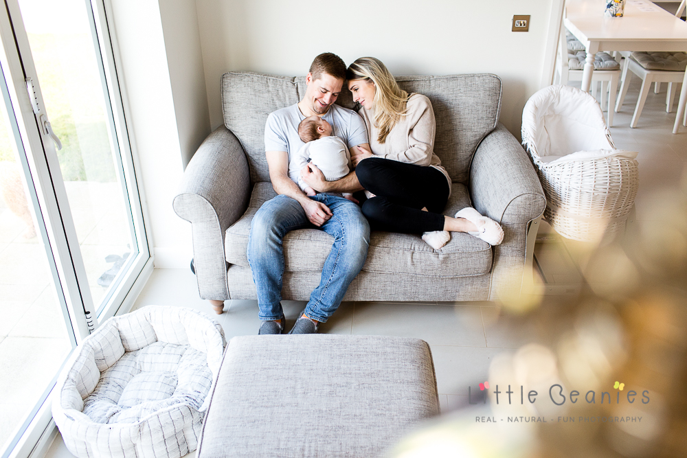 baby asleep with parents on sofa during newborn photoshoot at home in relaxed environment