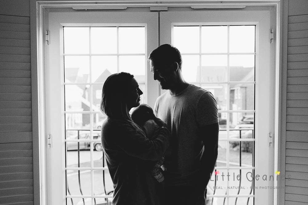 silhouette of mum, dad and baby in window having a cuddle on newborn baby photoshoot